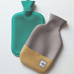 Puede incluir: Una botella de agua caliente de goma de color turquesa con una funda de tela gris y amarilla. La funda tiene un peque&ntilde;o logotipo con la palabra "TINDY" en ella.