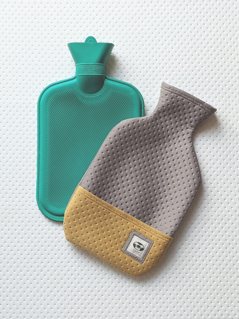 Puede incluir: Una botella de agua caliente de goma de color turquesa con una funda de tela gris y amarilla. La funda tiene un peque&ntilde;o logotipo con la palabra "TINDY" en ella.