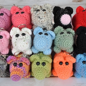 Puede incluir: Una colección de 15 llaveros de cerdo de crochet en varios colores, incluyendo rosa, rojo, azul, verde, negro y blanco. Cada llavero tiene un pequeño anillo de metal para sujetar las llaves.