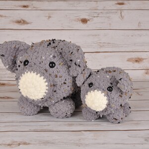 Puede incluir: Dos peluches de cerdo gris hechos a crochet con hocicos blancos y ojos negros. El cerdo más grande está de pie detrás del más pequeño.
