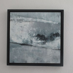 Op de afbeelding: Abstract schilderij in een zwarte lijst. Het kunstwerk heeft een textuur met grijstinten, wit en zwart. De compositie bevat horizontale en diagonale lijnen, waardoor een landschapseffect ontstaat. Het vierkante schilderij is gemonteerd in een zwarte lijst.