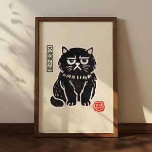 Può includere: Stampa artistica incorniciata raffigurante un gatto nero con un'espressione scontrosa. L'illustrazione del gatto ha accenti bianchi su uno sfondo color crema. Il testo giapponese è a sinistra e un timbro rosso in basso a destra. La cornice è marrone.