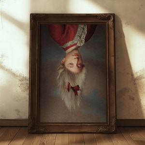 May include: A framed portrait of a person in a red jacket with white trim, depicted upside down. The person has light-coloured hair tied with a red bow. The portrait is in a dark wooden frame, leaning against a wall.