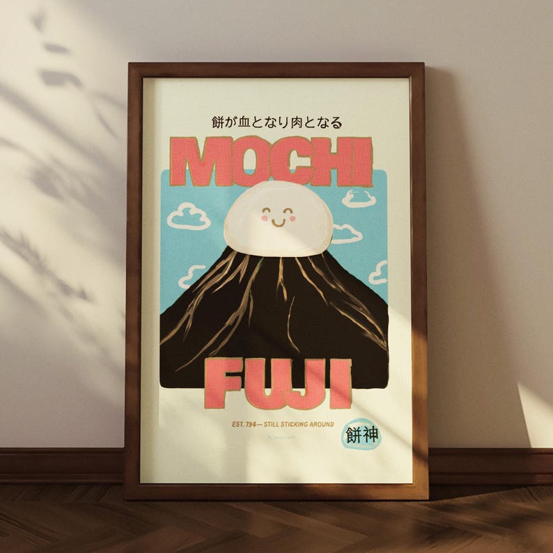 May include: A framed art print featuring a whimsical illustration of Mount Fuji with a mochi-shaped cloud. The text reads "MOCHI FUJI" in coral letters, with Japanese text above and below. The artwork is set against a light blue sky with cartoon clouds.