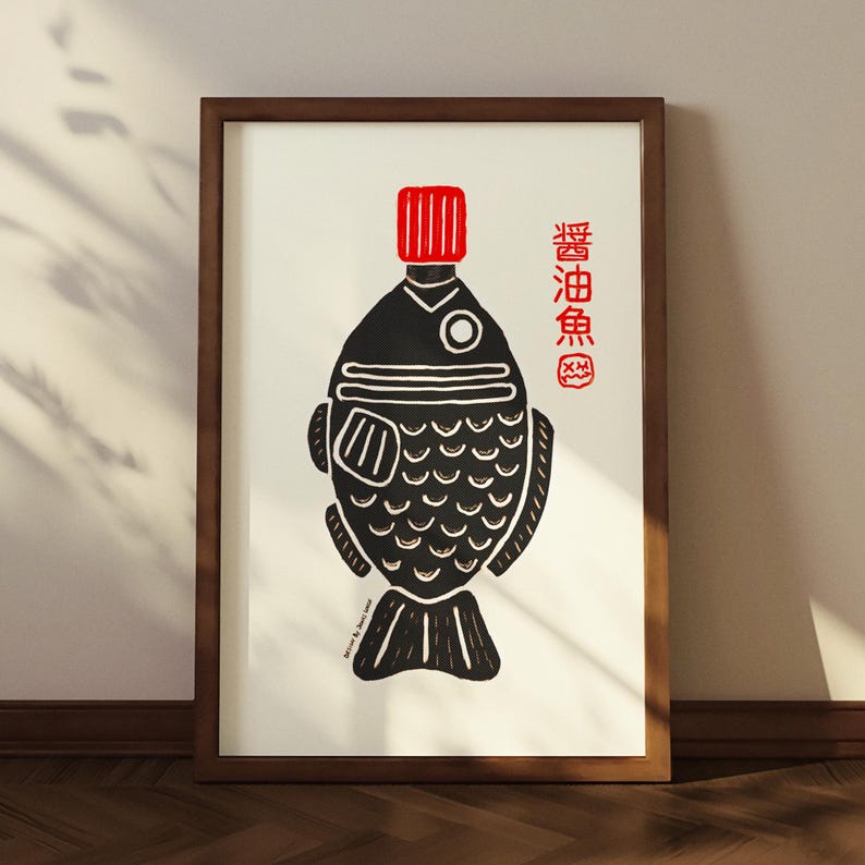 以下が含まれることがあります： 魚の形をした醤油ボトルの白黒イラストが描かれた、額装されたアートプリント。ボトルには赤いキャップがあり、右側には日本語のテキストがあります。アートワークは茶色の木製フレームに入っています。
