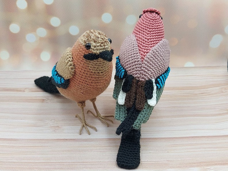 May include: Two crocheted bird toys, one brown with blue accents and one pink with brown, white, and green accents.
