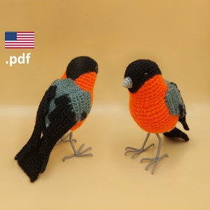 Op de afbeelding: Twee gehaakte amigurumi vogels. Een vogel is zwart, grijs en oranje. De andere vogel is zwart, oranje en grijs. De vogels zitten op een beige oppervlak. .pdf