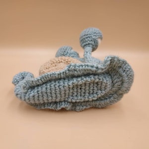Pu&ograve; includere: Un giocattolo a forma di lumaca in crochet blu e beige con un guscio testurizzato e tre protuberanze rotonde sul dorso.
