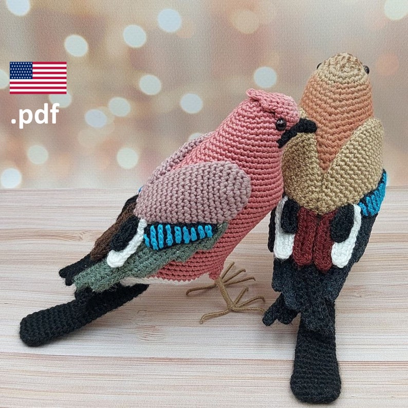 May include: Two crocheted amigurumi birds, one pink and one brown, with black, white, and blue details. The birds are sitting on a wooden surface.