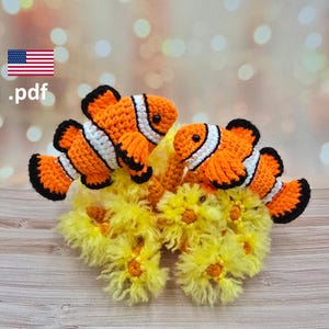 May include: Two crocheted clownfish, with orange bodies, white stripes, and black detailing, sit on a yellow, textured base. The image includes the American flag and the text ".pdf".