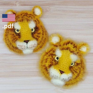 May include: Two crocheted tiger faces with yellow and brown fur, white noses, and black eyes. The tiger faces are on a wooden background.