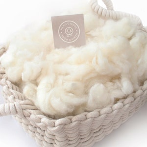 May include: A white woven basket filled with white merino wool. The basket has a rope handle and a label that reads "Merino Wool".