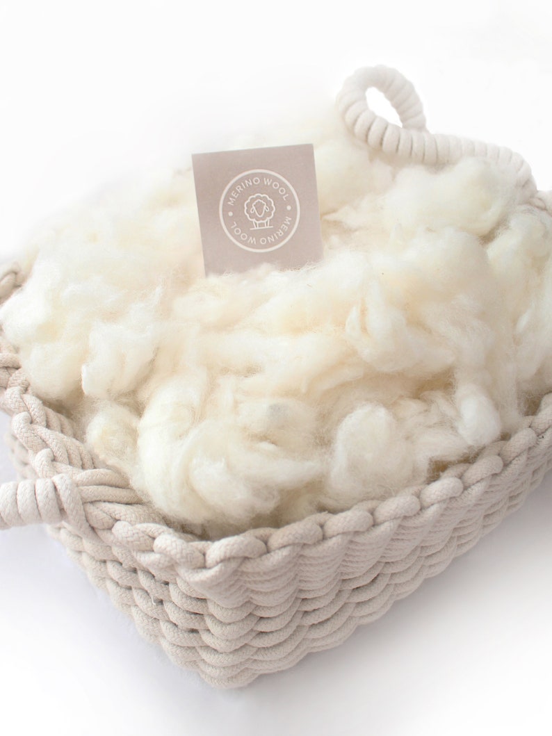 May include: A white woven basket filled with white merino wool. The basket has a rope handle and a label that reads "Merino Wool".