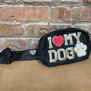 May include: Black fanny pack with a gold "I love my dog" design, a red heart, and a white paw print. The strap is black with white text.