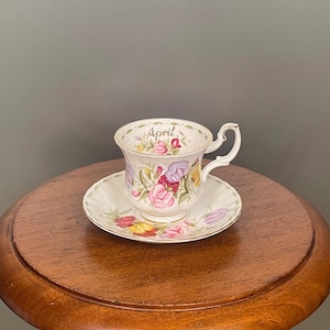 Peut inclure: Un service à thé vintage composé d'une tasse et d'une soucoupe avec des motifs floraux roses, violets et jaunes. La tasse et la soucoupe sont blanches avec des bordures dorées. Le mot "April" est écrit sur la tasse.