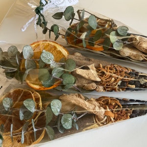 Peut inclure: Trois sachets en plastique transparents remplis de tranches d'orange séchées, de feuilles d'eucalyptus et d'autres ingrédients naturels. Les sachets sont attachés avec de la ficelle et portent une étiquette sur laquelle est inscrit "Joy".