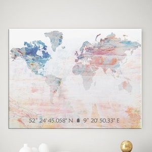 Könnte beinhalten: Ein weißer Leinwanddruck einer Weltkarte mit einem aquarellartigen Design in Blautönen, Rosa und Beige. Die Karte ist gerahmt und hängt an einer weißen Wand über einer weißen Kommode mit sechs Schubladen. Die Kommode steht in einem Wohnzimmer mit einem schwarzen Couchtisch und einer Topfpflanze.