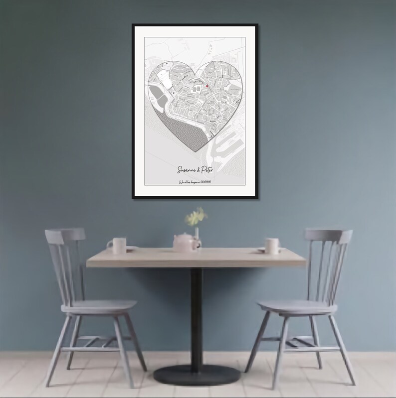May include: A black and white map of a city with a heart shape drawn over it. The heart shape is filled in with a red dot in the center. The text "Suzanne & Peter" and "July 1st, 2023" is printed below the map.