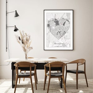 May include: A black and white map of a city in the shape of a heart with a red dot in the center. The map is framed and hanging on a white wall above a dining table with four chairs.
