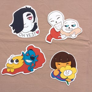 May include: Four colourful stickers featuring characters from a video game. One sticker shows a character with black hair and the text "OH YES!". Another shows two skeleton characters. A third sticker shows two characters, one with blue skin. The last sticker shows a character holding a flower.