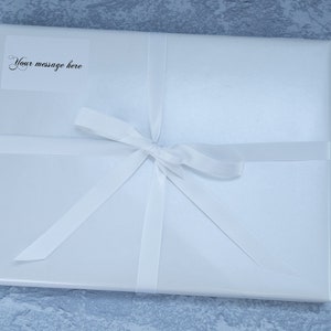 May include: A white gift box with a white ribbon tied in a bow. A small white label on the box says "Your message here".