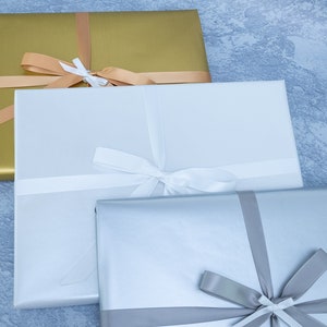 May include: Three gift boxes wrapped in different colors: gold, white, and silver. Each box is tied with a ribbon in a matching color.
