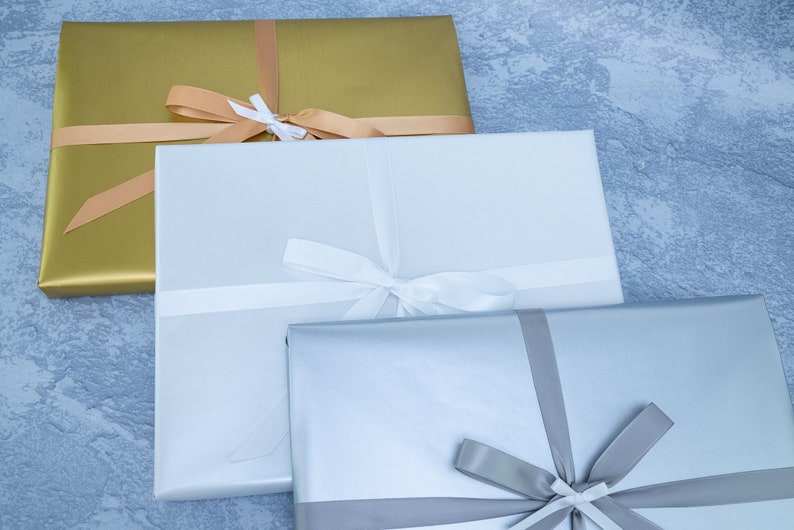 May include: Three gift boxes wrapped in different colors: gold, white, and silver. Each box is tied with a ribbon in a matching color.