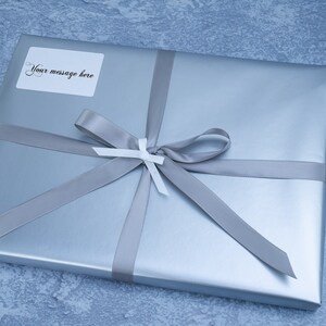 May include: A silver gift box with a gray ribbon and bow. A white label with the text "Your message here" is attached to the box.