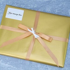 May include: A gold gift box with a beige ribbon and a white bow. A white label with the text "Your message here" is attached to the box.
