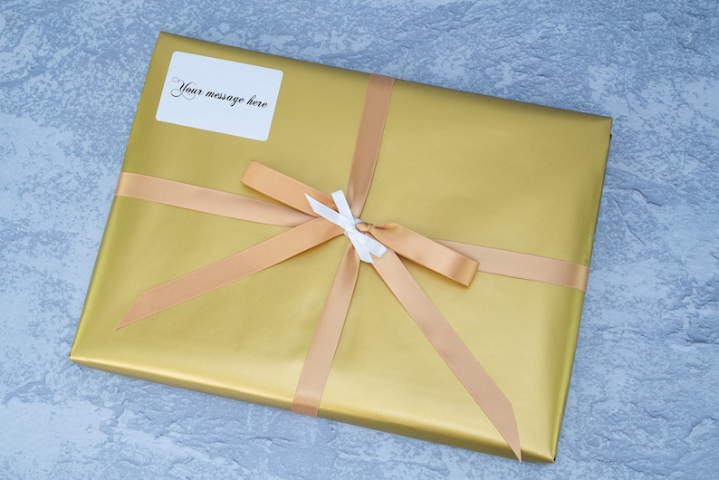 May include: A gold gift box with a beige ribbon and a white bow. A white label with the text "Your message here" is attached to the box.
