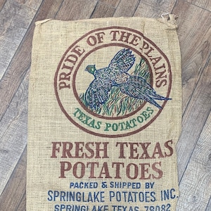 May include: A burlap potato sack with the text "Pride of the Plains" and "Texas Potatoes" in a circular design. Below, it reads "Fresh Texas Potatoes." The sack is printed with a pheasant illustration and the text "Springlake Potatoes Inc."