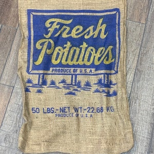 May include: A burlap potato sack with a blue and yellow graphic. The graphic reads "Fresh Potatoes" and "Produce of U.S.A." The sack is labeled "50 LBS - NET WT 22.68 KG".