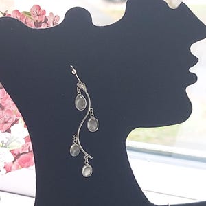 May include: Silver dangle earrings with four oval-shaped clear stones hanging from a curved silver wire.