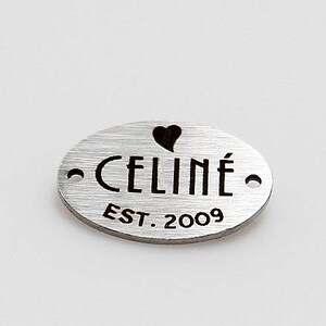 May include: Silver oval tag with the text "CELIN&Eacute; EST. 2009" and a small heart cutout.