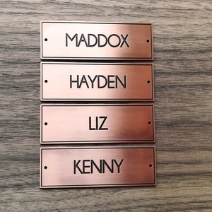 May include: Four copper-colored metal nameplates with black lettering. The names on the plates are Maddox, Hayden, Liz, and Kenny.