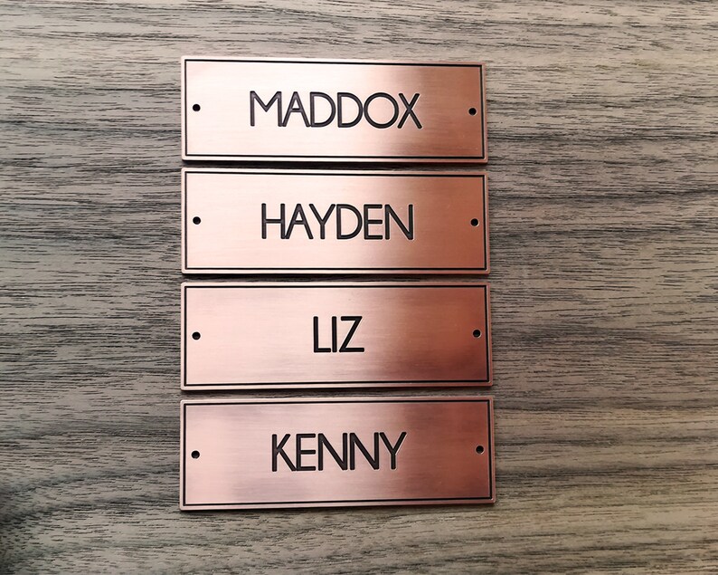 May include: Four copper-colored metal nameplates with black lettering. The names on the plates are Maddox, Hayden, Liz, and Kenny.