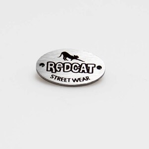 May include: Silver oval metal tag with a black silhouette of a cat and the text "REDCAT STREET WEAR".
