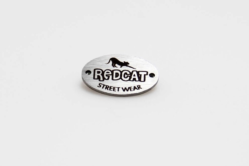May include: Silver oval metal tag with a black silhouette of a cat and the text "REDCAT STREET WEAR".