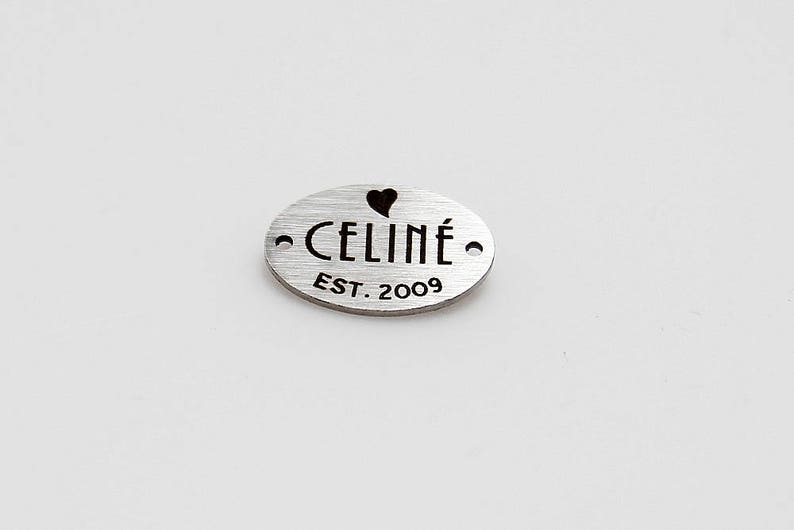May include: Silver oval tag with the text "CELIN&Eacute; EST. 2009" and a small heart cutout.