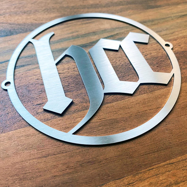 Op de afbeelding: Een zilveren metalen cirkel met het woord "HOC" in een gotisch lettertype.