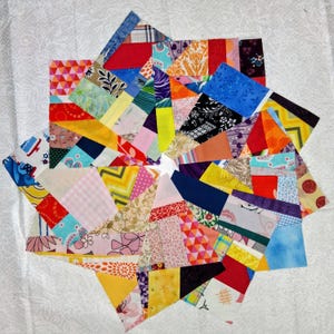 May include: A colorful, star-shaped quilt block composed of various fabric scraps. The patchwork design features a vibrant mix of patterns and colors, including red, blue, yellow, and pink. The block is set against a white background.