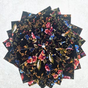 May include: A collection of square fabric swatches arranged in a circular fan pattern. Each piece features a black background with a vibrant floral print consisting of red, pink, blue, and yellow flowers, green leaves, and thin brown branches.