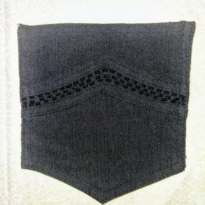 May include: A dark denim pocket with a decorative beaded design along the top edge. The pocket is rectangular with a curved bottom and is likely from a shirt or jacket.