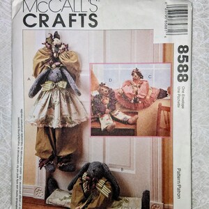 May include: McCall's Crafts sewing pattern envelope 8588 featuring illustrations of stuffed rabbit dolls. The pattern includes designs for rabbits wearing dresses, pants, and shirts with various fabric textures and patterns, labeled A, B, C, and D.