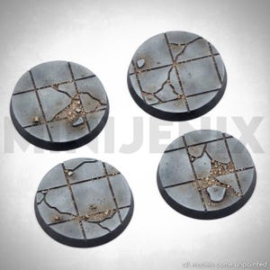 May include: Four circular miniature bases featuring a grey tiled floor pattern with cracks, debris, and rubble textures. Each base has a smooth black rim and a weathered stone appearance. The text all models come unpainted is visible.