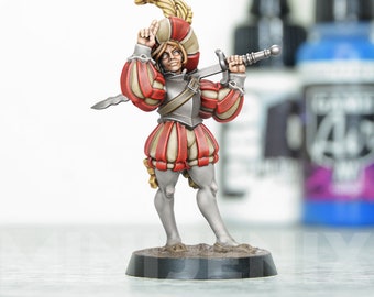 May include: A painted miniature figurine of a person wearing a red and white striped outfit, a feathered hat, and holding a sword. The figurine is standing on a black base.