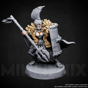 May include: A grey and gold painted miniature figurine of a female warrior with a lion head shield, a spear, and a helmet with a plume. The figure is standing on a grey round base.