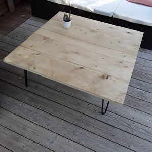 Pu&ograve; includere: Un tavolino da caff&egrave; in legno chiaro con finitura naturale e gambe a forcina nere. Il tavolino &egrave; su un ponte in legno.