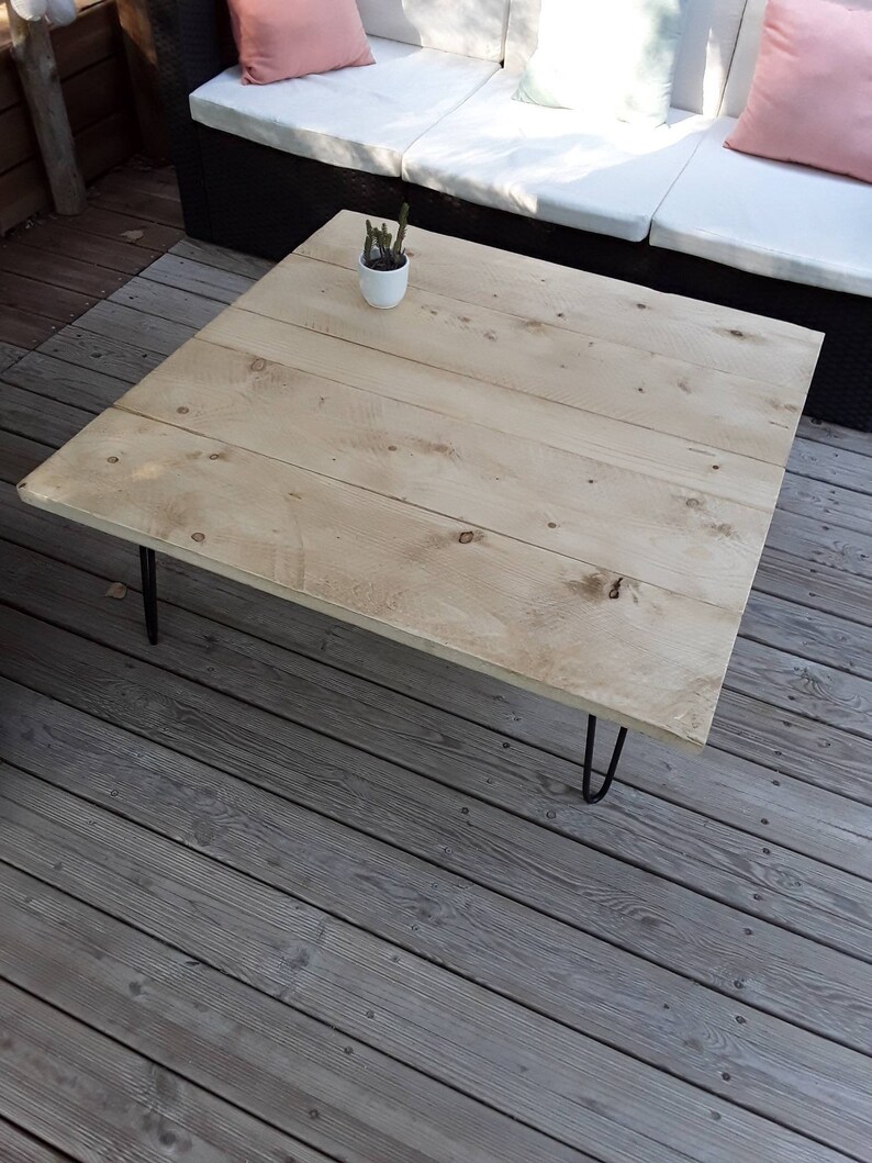 Pu&ograve; includere: Un tavolino da caff&egrave; in legno chiaro con finitura naturale e gambe a forcina nere. Il tavolino &egrave; su un ponte in legno.