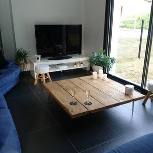 Puede incluir: Una sala de estar con un sof&aacute; seccional azul, una mesa de caf&eacute; de madera grande con dos copas de champ&aacute;n y un taburete blanco. La habitaci&oacute;n tiene una ventana grande con vista a un c&eacute;sped verde y una cerca negra.